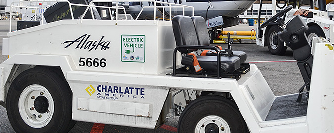 Photo of a white Alaska Air Group Charlatte America eGSE belt loader in front of a white Alaska Air plane.