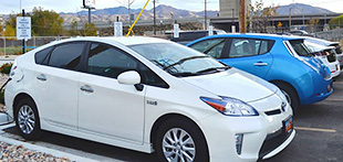 Three electric sedans plugged into charging equipment at outdoor parking spaces.