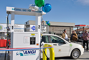 Photo of a white car parked in front of a white CNG fueling station with balloons tied to the top.