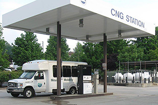 Photo of a white shuttle bus parked in front of a refueling station for CNG.